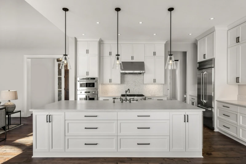 Fix & Flip Home Loan 1 Modern white kitchen with large island featuring drawers, pendant lighting, stainless steel appliances, white cabinets, and dark hardware, set on a wooden floor with a clean, minimalist design.