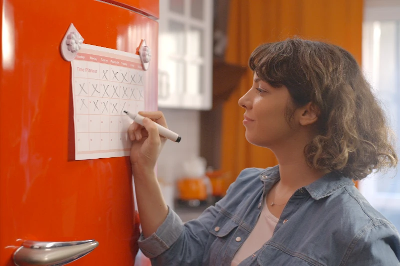 Blog 12 Woman marking off her calendar hanging on a fridge